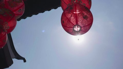 The red Chinese lanterns hanging in front of the gate of Chinese temple are swaying in the wind and passing by the sunlight.The meaning of the words on the lanterns are luck ,happiness and rich.