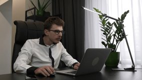 Focused smart man in glasses is using laptop in modern office. Businessman is working on computer at home workplace. Employee works on laptop, looking at screen and typing on keyboard at office desk