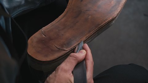 Close-up shoemaker cuts knife through leather sole at production shoes. Shoemaker sews shoes. Craft production. Cinematic light