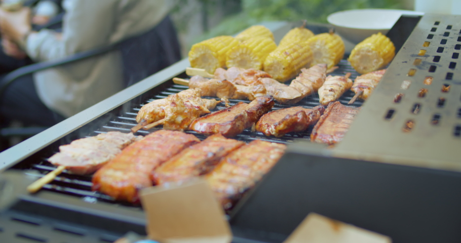Spare ribs and chicken sticks spears with sweet corn grill on steaming bbq in flames. Friends have bbq party at backyard cookout, have fun with healthy and locally sources ingredients  Royalty-Free Stock Footage #1058218210