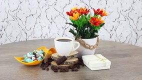 Coffee cup with colored rocks with flowers on spinning wooden table background.