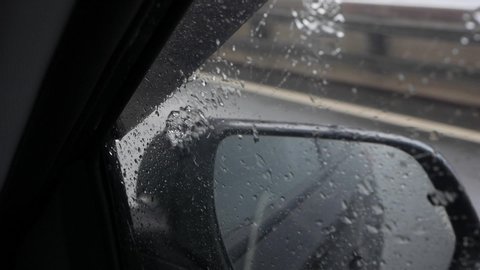 View out the rear view mirror as car drives on highway in the rain