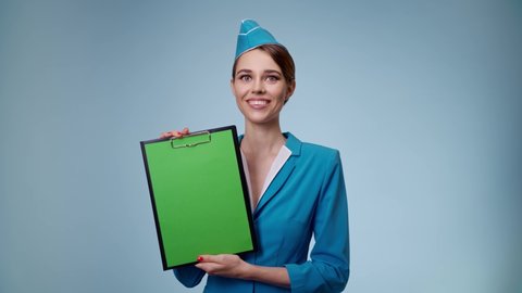 Attractive stewardess holding tablet with blank green sheet. Blue background.