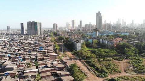 An aerial drone movement shot of the large closely packed urban slums or shanty town while skyscrapers or tall building situated in the background in the Mumbai city