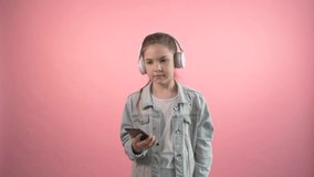 Cute girl is listening in headphones listening to music and dancing. Nice fun music. Pink background.