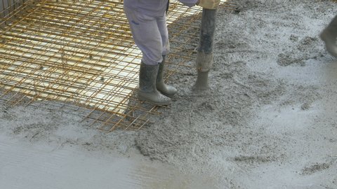 CLOSE UP: Unrecognizable team of workers pours fresh mortar over metal wiring covering the ground floor of a modern house under construction. Contractor pours wet mortar across the ground floor.