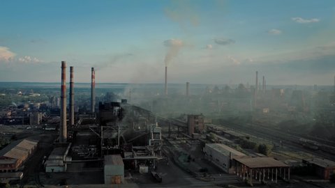 Drone shot of industrial zone with thick smog and burning fossil fuels. Factory zone pan shot left to right of polluted city, many factory chimneys in city area