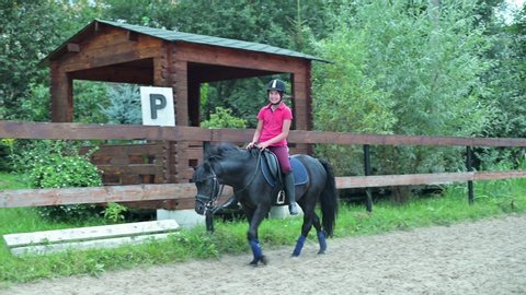 smiling teenage girl in a helmet rides a black horse in a special paddock
