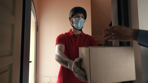 An young mailman courier with a protective mask and gloves is delivering a parcel directly to a customer home with safety. Concept of courier, home delivery, e-commerce shipping, virus, covid