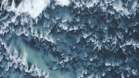Aerial drone top down view at strong streams of cold blue water from waterfall at Iceland, 4k Beautiful pattern od ice, water and foam.