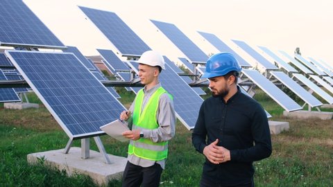 New business with solar panels under the blue sky. Two charismatic workers in special outfits walk around and talk about installing solar cells. Modern solar panels produce organic electricity.