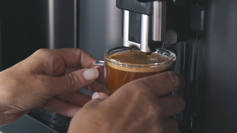 Close up of espresso coffee flowing in thin stream from professional coffee machine in glass cup. Automatic coffee machine making fresh americano coffee in morning