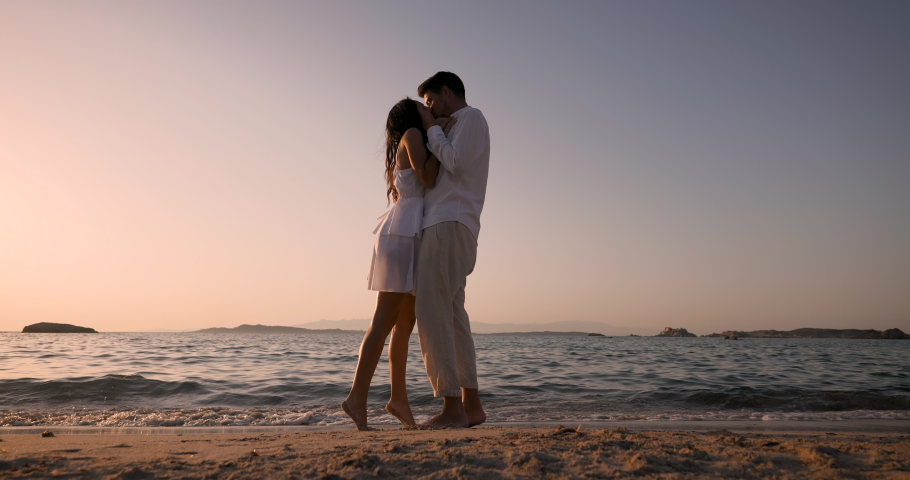 Authentic shot of  an young carefree  happy couple is hugging and kissing while enjoying their summer holidays romantic vacation together on a seaside beach at sunset.