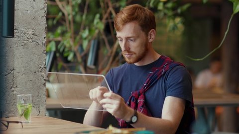 Red-haired start-up entrepreneur using holographic tablet internet device for communication browsing social media hologram user interface inside cafe interior.