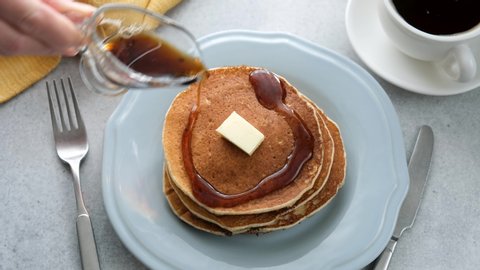 Pouring maple syrup on pancakes with butter. American style breakfast