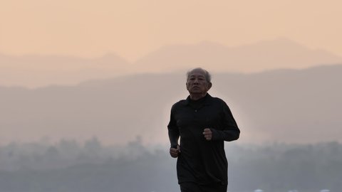 Front view Asian elderly exercise. Senior man running on road In the morning with the sunrise behind Slow Motion. health lifestyle and exercise Concept
