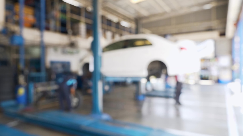 Blurred Background of Technicians Car Repair Center with Mechanics and Electric Lift for Cars in Service Station. Electric Lift Is Lifting the Car Up and Worker Removing Tire. Defocused Video | Shutterstock HD Video #1058241127