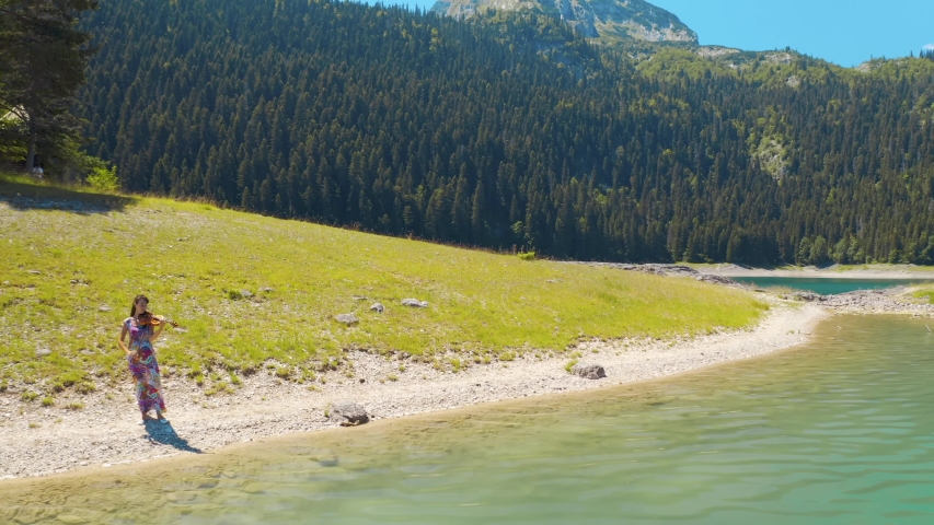 Aerial panoramic view of the young woman professional violin player is standing near turquoise water of the Black Lake in Montenegro