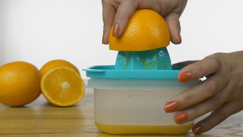 Closeup shot of woman hands squeezing out fresh orange juice on a manual juicer. Hands of an Indian female juicing orange fruit on a manual plastic squeezer against the white background