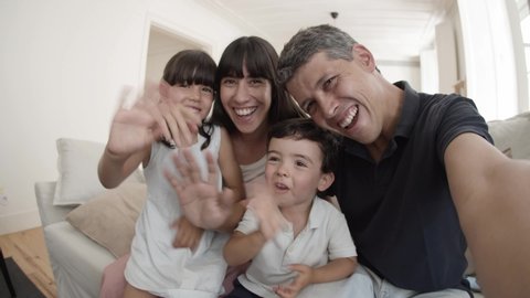 Happy family using phone for video call, two cute kids smiling and waving hello at camera, dad holding gadget. Pov shot. Communication concept