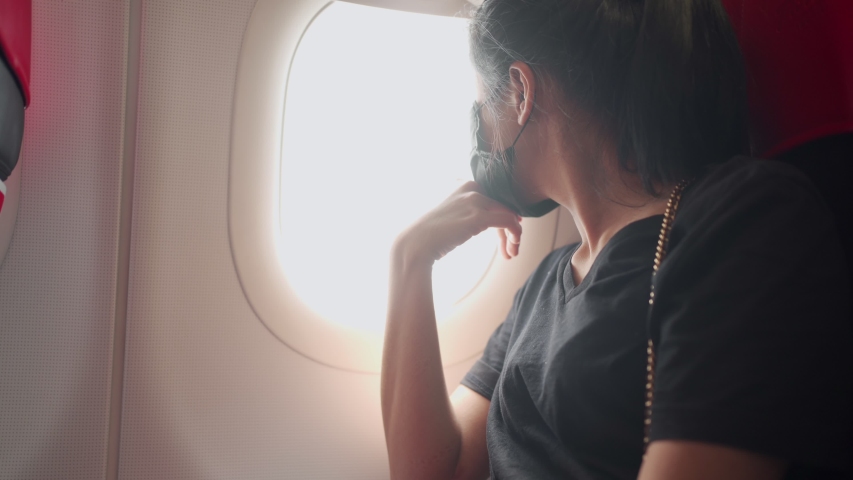 Female airplane passenger looking out through the window, Asian woman sitting at window seat on the plane, curiosity safety concern,  covid-19 new normal travel social distancing, , pandemic crisis | Shutterstock HD Video #1058252518