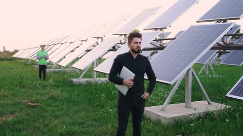 Portrait of the Caucasian industrial worker standing on an ecological field of solar panels. Alternative energy. Solar energy generation. The concept of ecology. In the background is a worker.