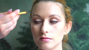 Video of making makeup. Make-up artist applied with brush on model face. Portrait of young ginger woman in beauty salon. Hand of make-up master with brush make perfect skin and color eyeshadow. 4k 