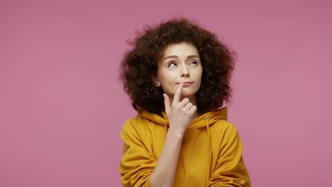 Cunning young woman afro hairstyle in hoodie thinking devious tricks cheats, twiddle fingers smirking and scheming evil plan, trying to plot something sly in mind.  isolated on pink background