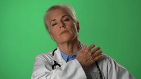 Portrait of experienced gray haired female doctor showing a patient how to relieve shoulder pain. Shot on green screen.