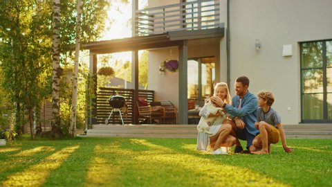Smiling Father, Mother and Son Pet and Play with Jack Russell Terrier Retriever Dog. Sun Shines on Idyllic Happy Family with Loyal Pedigree Dog have Fun at the Idyllic Suburban House Backyard