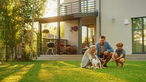 Smiling Father, Mother and Son Pet and Play with Jack Russell Terrier Retriever Dog. Sun Shines on Idyllic Happy Family with Loyal Pedigree Dog have Fun at the Idyllic Suburban House Backyard