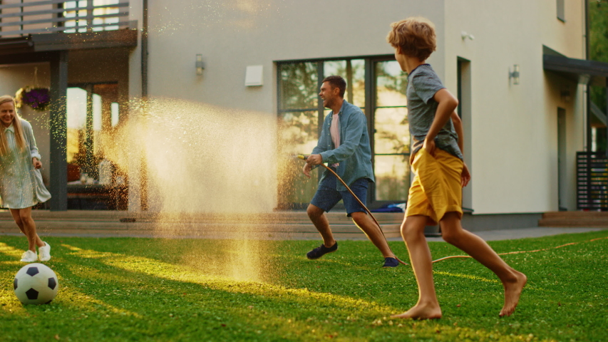 Happy Family of Four Playing with Garden Water Hose, Spraying Each Other. Mother, Father, Daughter and Son Have Fun Playing Games in the Backyard Lawn of Idyllic Suburban House on Sunny Summer Day Royalty-Free Stock Footage #1058261899
