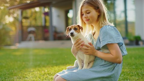 Cute Girl Holds Her Favourite Pedigree Dog Friend while Having Picnic Outdoors on the Lawn. She Pets and Cuddles Her Little Jack Russell Terrier. Idyllic Summer House. Slow Motion