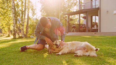 Handsome Young Man Wrestles with His Loyal Golden Retriever Dog, Scratches His Head, Cuddles, Plays with Man's Best Friend. Gorgeous Sunny day, Having Fun Outdoors