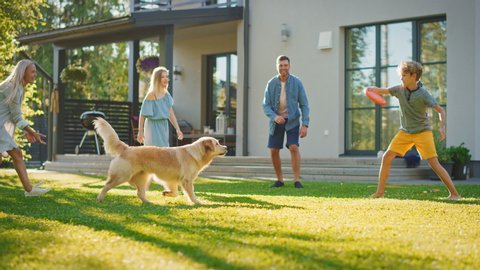 Smiling Beautiful Family of Four Play Fetch Frisbee with Happy Golden Retriever Dog on the Backyard Lawn. Idyllic Family Has Fun with Loyal Pedigree Dog Outdoors in Summer House Backyard. Slow Motion