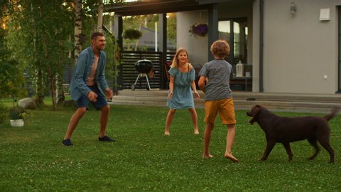 Beautiful Family of Three Play Fetch Toy Ball with Happy Brown Labrador Retriever Dog on the Backyard Lawn. Idyllic Family Has Fun with Loyal Pedigree Dog Outdoors in Summer House