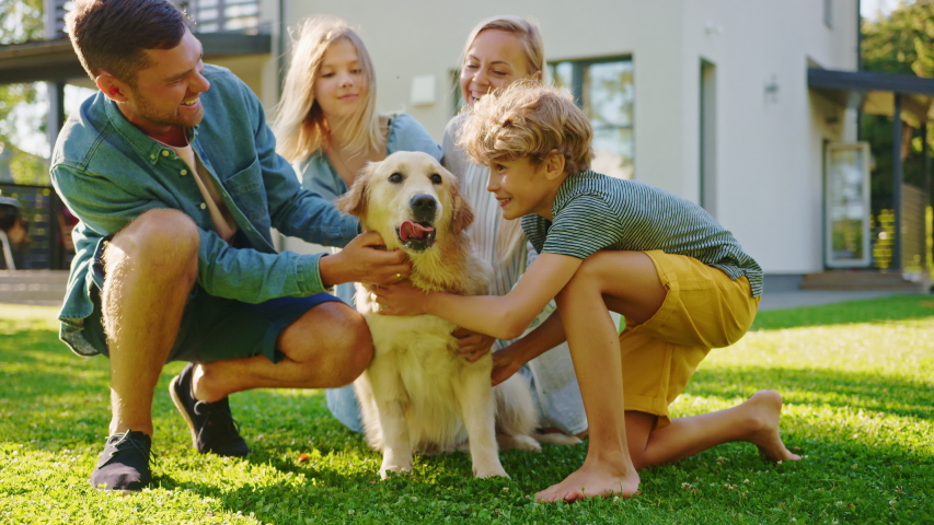 Smiling Beautiful Family of Four Posing with Happy Golden Retriever Dog on the Backyard Lawn. Idyllic Family Cuddling Loyal Pedigree Dog Outdoors in Summer House Backyard. Slow Motion Shot Royalty-Free Stock Footage #1058262175