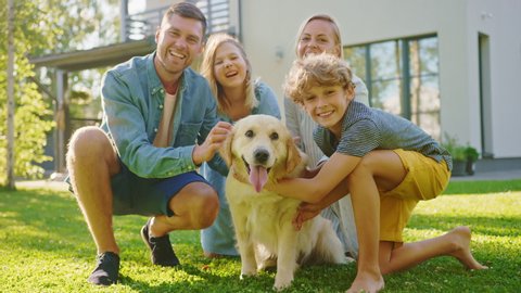 Smiling Beautiful Family of Four Posing with Happy Golden Retriever Dog on the Backyard Lawn. Idyllic Family Cuddling Loyal Pedigree Dog Outdoors in Summer House Backyard. Slow Motion Shot
