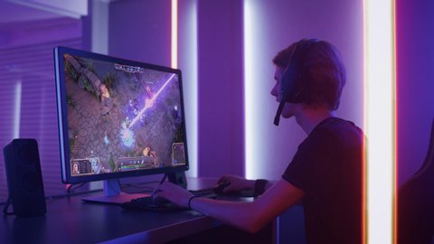 Professional eSports Gamer Plays RPG MOBA Mock-up Video Game with Super Action and Fun Special Effects on His Personal Computer, Talks to Teammates using Headset. Cyber Gaming Stylish Retro Neon Room