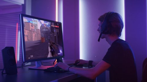 Professional eSports Gamer Skilfully Plays 3D Shooter Mock-up Video Game with Super Action and Fun Special Effects on His Computer, Talks to Teammates using Headset. Cyber Gaming Retro Neon Room