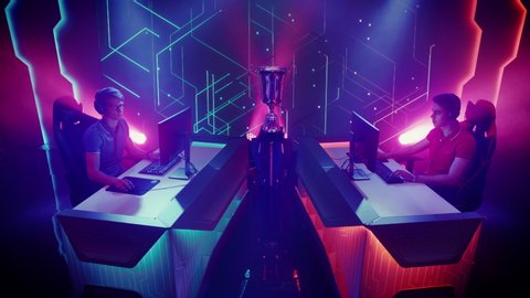 Two Professional Esport Gamers Actively Compete in a Video Game Playing on a Championship Event with Big TV Screens and Stylish Neon Arena. Cyber Gaming Tournament. Elevated Crane Static Camera Shot