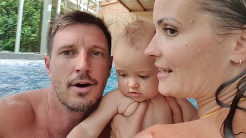 A happy family with a baby boy taking a selfie and having fun at a pool. 4K