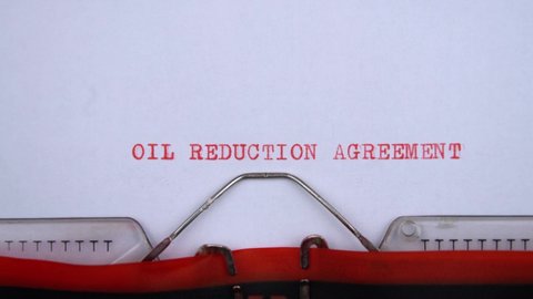 Oil reduction agreement. phrase printed on an old typewriter in red letters, close up. vintage inscription