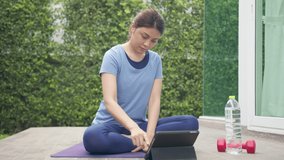 Asian sporty woman choosing online tutorials workout and yoga on internet channel in taplet device before exercise and stretching. Activity during quarantine and social distance new normal concept.