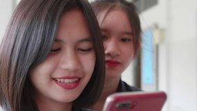 Slow motion of two young Asian girls who are close friends, smiling, laughing and having fun on social media on smartphone.