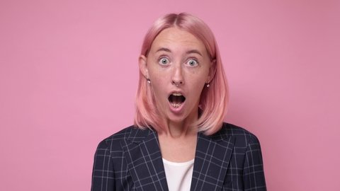 Beautiful caucasian surprised woman being shocked with news covering mouth saying wow. Studio shot on pink wall.