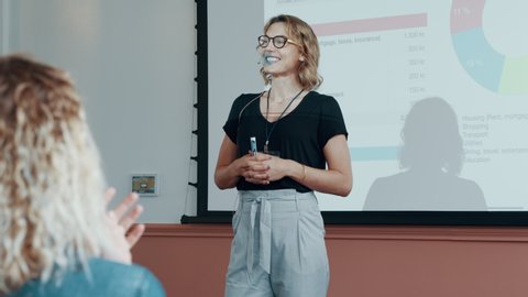 Businesswoman standing in front of a projection screen and presenting her ideas to group of people sitting in a seminar. Female professionals addressing a business conference.
