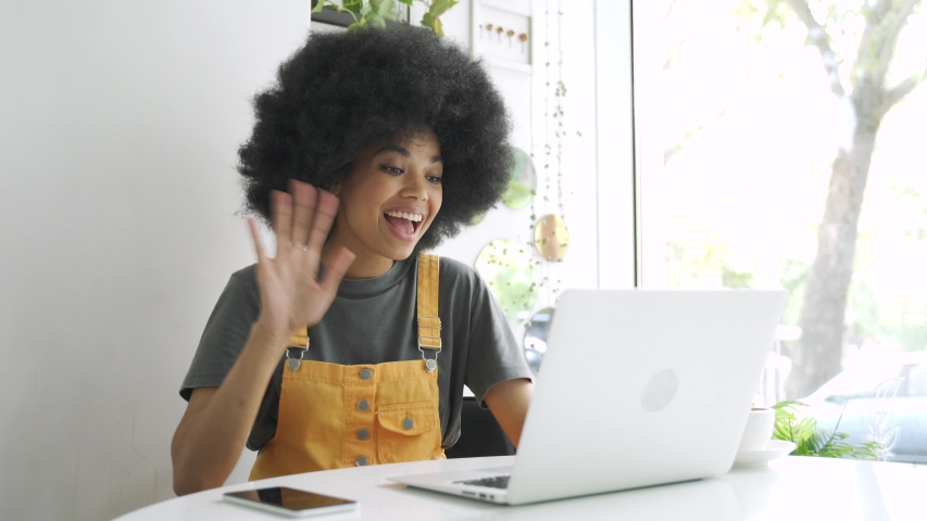 Happy hipster African American gen z woman, female student with afro hair talking with friend using laptop computer video conference calling in virtual webcam online chat sitting at table in cafe. Royalty-Free Stock Footage #1058278537