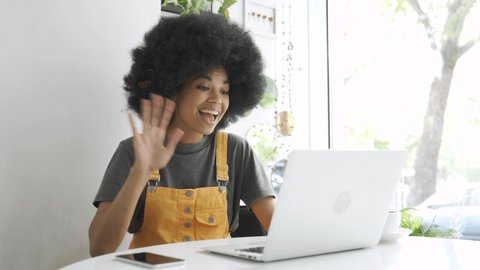 Happy hipster African American gen z woman, female student with afro hair talking with friend using laptop computer video conference calling in virtual webcam online chat sitting at table in cafe.