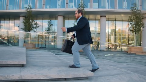 Fat businessman in formal suit running up stone stairs near office building being late. Overweight office manager hurry to business meeting with clients running near business center